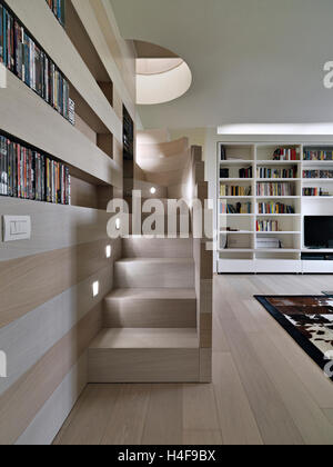modern living room in foreground the wooden staircase overlooking on the big bookcase whose floor is made of wood