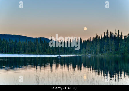 Full moon over a lake in a forest  of Sweden, during sunset Stock Photo
