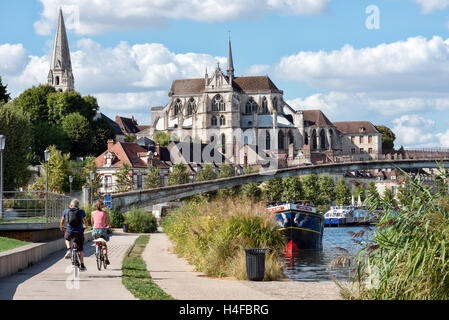 Visitors cycling towards Abbaye de Saint-Germain d'Auxerre in Auxerre on the towpath beside the river Yonne, Burgundy , France Stock Photo