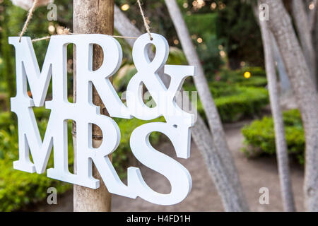 Mr and Mrs White Wedding letters hanging sign from wooden pole with garden on background Stock Photo