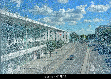 Shattered concept vision of a main road & Tesco Store in Slough Berkshire UK as seen through a crazed broken glass window pane on a blue sky sunny day Stock Photo