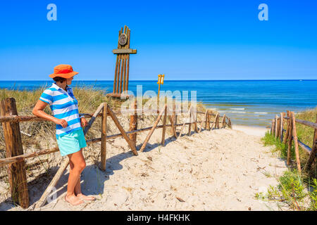 Young woman tourist wearing a hat standing at entrance to idyllic sandy beach in Bialogora coastal village, Baltic Sea, Poland Stock Photo