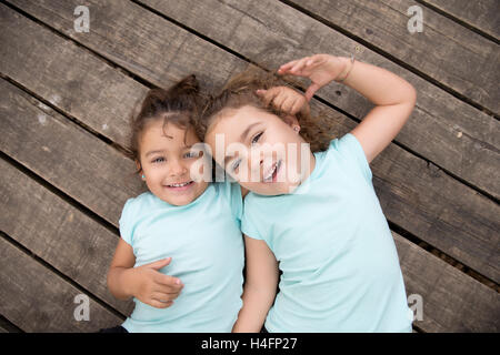 Top view portrait of cute smiling sisters in similar blue t-shirts lying on wooden background Stock Photo