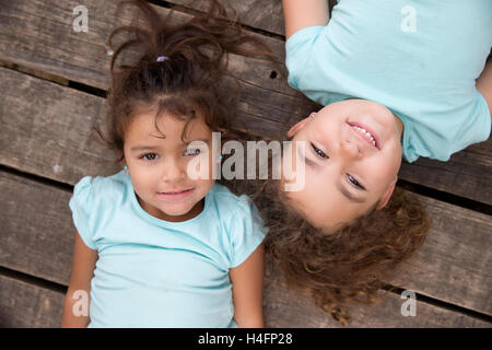 Top view of two pretty girls with curly hair looking at camera with smile over wooden background. Stock Photo