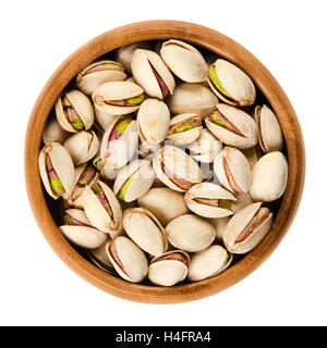 Roasted pistachio seeds with shell in wooden bowl on white background. Pistacia vera fruits and kernels. Isolated macro photo. Stock Photo