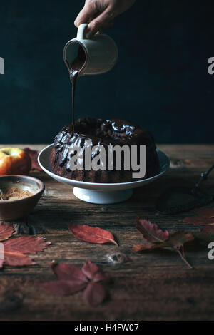 Carob and apple bundt cake on a cake stand and female hand drizzling chocolate ganache Stock Photo