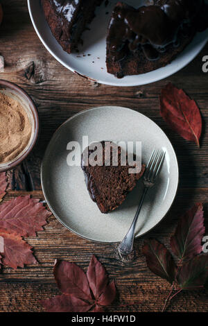 Carob and apple bundt cake with chocolate ganache on a cake stand and a cake slice on dessert plate Stock Photo