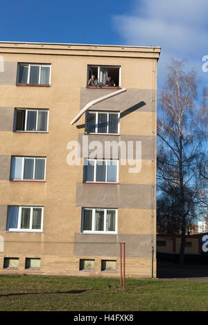 Two seniors throwing rolled carpet out of a window from the top floor of a building. Stock Photo