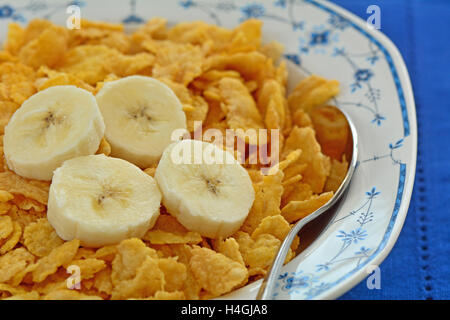 Crisp golden organic corn flakes with banana slices in pretty blue and white bowl on vibrant blue napkin in horizontal format. Stock Photo
