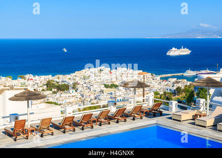 MYKONOS ISLAND, GREECE - MAY 17, 2016: Sunbeds alongside of a hotel pool and view of Mykonos town, Cyclades islands, Greece. Stock Photo