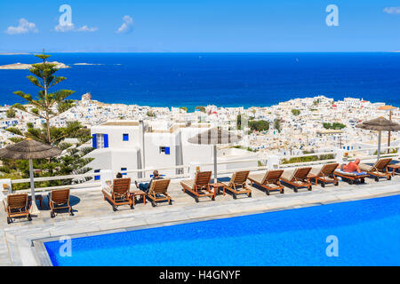 MYKONOS ISLAND, GREECE - MAY 17, 2016: Sunbeds alongside of a hotel pool and view of Mykonos town, Cyclades islands, Greece. Stock Photo