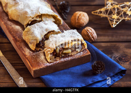 Christmas homemade pastry. Apple strudel (pie) with raisins, walnuts and powdered sugar with Christmas decor close up. Stock Photo