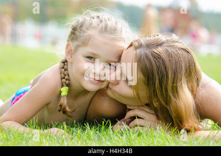 Mother kissing her daughter lying on a green grass lawn Stock Photo