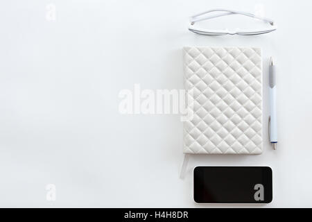 White office desk with glasses, mobile phone and pen Stock Photo