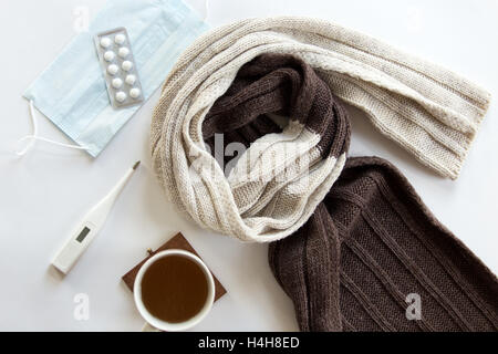 White desk with pills, thermometer, hot drink and a scarf on it Stock Photo