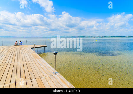 Couple of tourists sitting on a wooden pier in Chalupy village at Baltic Sea, Hel peninsula, Poland Stock Photo