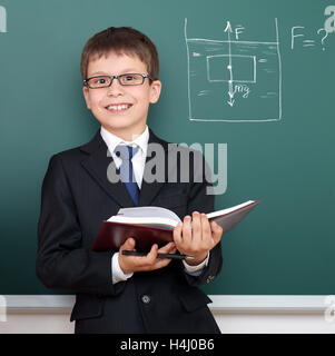 school boy with book, archimedes principle drawing on chalkboard background, dressed in classic black suit, education concept Stock Photo