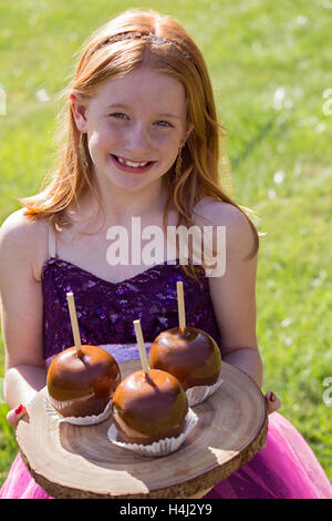 Happy girl dressed up in fairy Halloween costume and holding tray of caramel candy apples Stock Photo