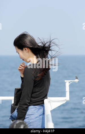 young asian woman with waving long hair looking at the sea from the deck of cruise ship Stock Photo