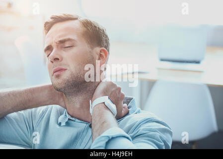 Tired young man which having a pain in his neck. Stock Photo