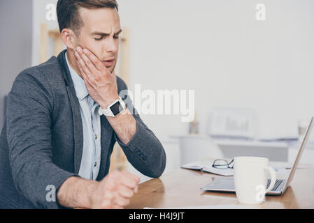 Handsome busy man having toothache on the work place. Stock Photo
