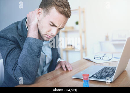 Exhausted young man suffering from pain in the neck Stock Photo