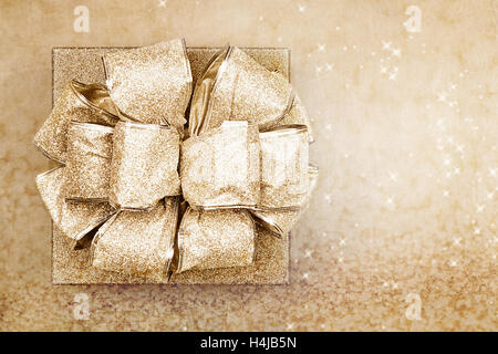 Beautiful gold gift with bow against a magical golden background with copy space. Image shot from over head. Stock Photo