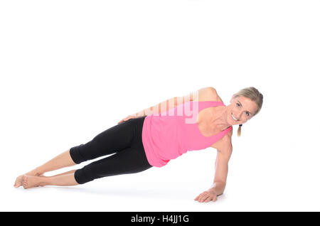 Smiling beautiful woman in pink top and black pants doing plank abdominal exercises over white background Stock Photo