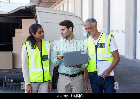 Manager and warehouse workers discussing with laptop Stock Photo