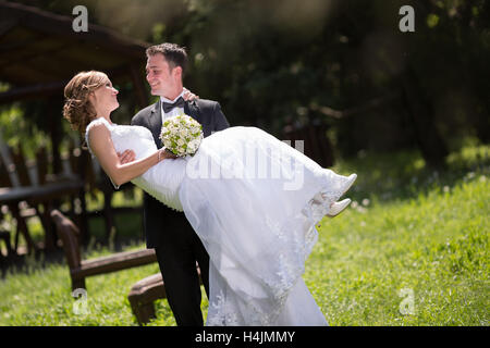 Groom carrying bride outdoors and smiling Stock Photo