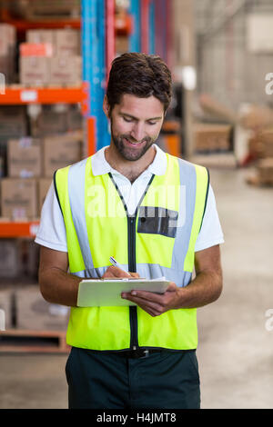 Happy warehouse worker writing on clipboard Stock Photo