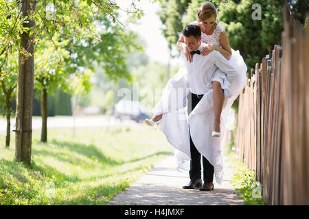 Groom carrying bride piggyback outdoors Stock Photo