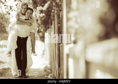 Groom carrying bride piggyback outdoors Stock Photo