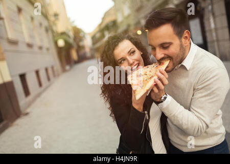 Couple eating pizza outdoors and smiling Stock Photo
