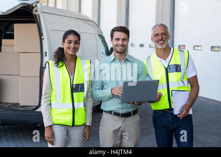 Manager and warehouse workers standing with laptop and clipboard Stock Photo