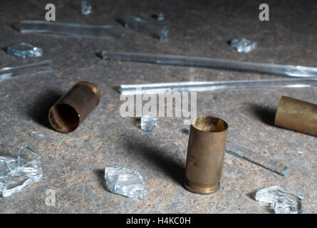 Handgun brass laying on dark concrete with broken glass Stock Photo