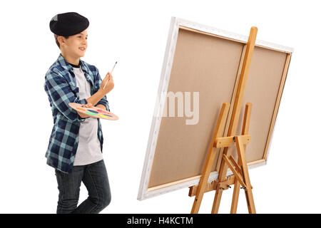 Little boy looking at a canvas and holding a paintbrush and a color palette isolated on white background Stock Photo