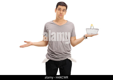 Sad young man showing his empty pockets and  holding a small empty shopping basket isolated on white background Stock Photo