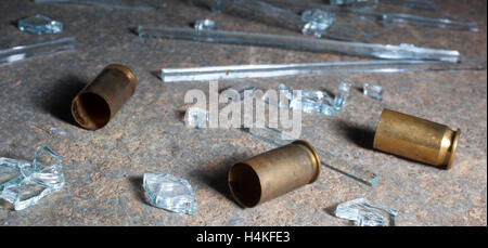 Handgun casings that are surrounded by glass on dark concrete Stock Photo