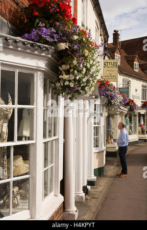 England, Berkshire, Hungerford, Bridge Street, customer looking in antique shop window below hanging baskets Stock Photo