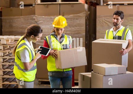 Manager noting on digital tablet while workers carrying cardboard boxes Stock Photo