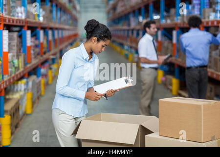 Female warehouse worker with a clipboard checking the boxes Stock Photo