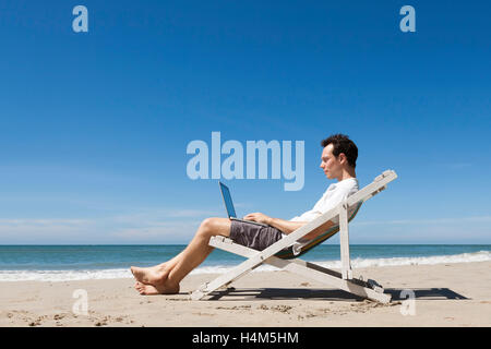 Happy young freelancer working online with laptop on a sunny tropical beach Stock Photo