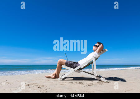 Freelancer working remotely with laptop and resting on sunny tropical beach, sunglasses Stock Photo