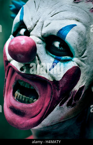 closeup of a scary evil clown with his mouth open showing his rotten teeth staring at the observer Stock Photo