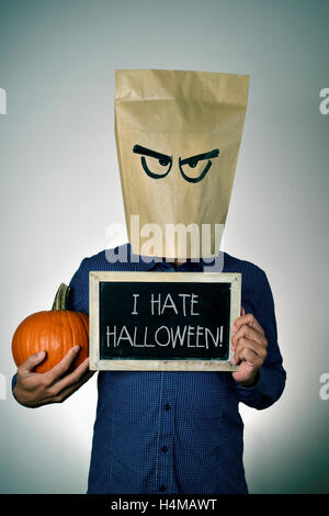 a young man with a paper bag in his head with a funny face, holds a pumpkin in his hand and shows a chalkboard with the text I h Stock Photo