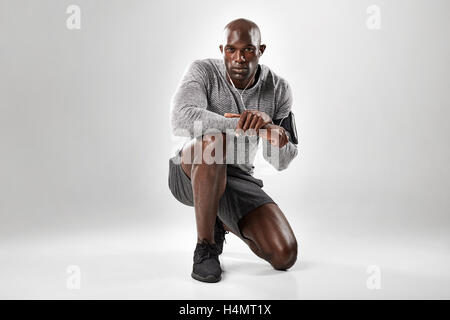 Portrait of fit young african man kneeling on grey background and looking at camera. Stock Photo