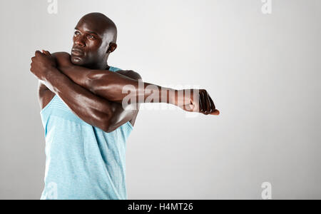 Fit young african man with muscular build stretching arms against grey background. Afro american fitness male model warming up. Stock Photo