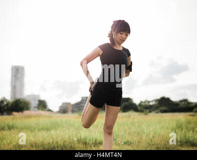 Shot of fit young woman stretching her legs at urban park. Chinese female model in sportswear doing warm up workout at a park in Stock Photo