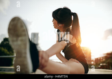 Shot of young woman stretching her legs after a run in the city. Female runner exercising in morning. Stock Photo